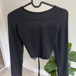 Svart långärmad snörningstopp Shein - Svart långärmad topp från Shein med croppad passform och snygg snörning framtill som kan justeras för att skapa en rynkad effekt. 