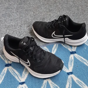 Svarta Nike Downshifter sneakers - Svarta Nike Downshifter sneakers med vit sula och klassisk vit swoosh på sidan. Ovandelen är i mesh för bra andningsförmåga och skon har snörning. Perfekta för dig som gillar sportig stil och vill ha bekväma skor till vardagen eller träningen.