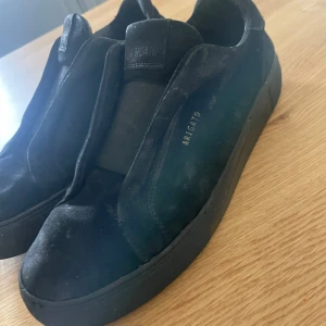 Svarta sneakers från Axel Arigato mocka - Stilrena svarta sneakers från Axel Arigato i mjuk mocka med diskret logga i guld på sidan. Skorna har elastisk panel över vristen istället för klassisk snörning, vilket ger en clean och modern look. Perfekta för dig som gillar minimalistisk stil. Priset kan diskuteras!😃