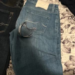 Två par jeans i olika blå nyanser - Säljer två par jeans, ett par i ljusblå tvätt med vit patch och ett par i mörkblå tvätt med svart patch. Båda har klassiska bakfickor med kontrastsömmar och är i rak modell. Perfekta för dig som gillar stilrena och tidlösa jeans.