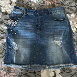 Jeanskjol - Snygg blå jeanskjol från MYHAILS med slitna detaljer, fransad nederkant och pärl- och stenapplikationer på ena sidan. Klassisk femficksmodell med bälteshällor och dragkedja. Perfekt för dig som vill ha en cool och trendig look. Kjolen är knappt än ändå. Skriv vid frågor 🤩