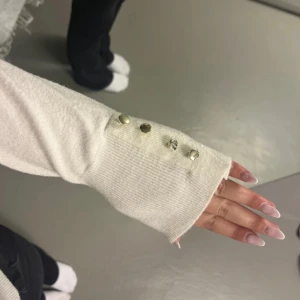 Vit tröja från Amisu - Säljer en stilren vit tröja från Amisu med långa ärmar och dekorativa knappar vid ärmsluten. Perfekt för en elegant look. Tröjan är tillverkad i ett mjukt material💕.