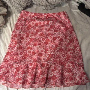 Rosa blommig kjol från Fransa - Säljer en söt rosa kjol från Fransa med blommigt mönster. Kjolen har en volangdetalj längst ner. Perfekt för sommaren