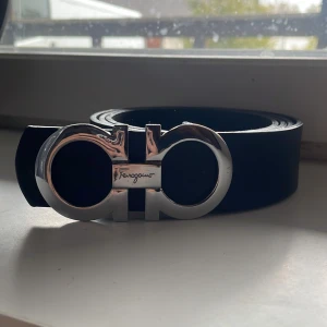 Silver Ferragamo bälte  - Snyggt svart bälte från Ferragamo med en iögonfallande silverfärgad spänne. Perfekt för att ge en stilren touch till din outfit. Bältet har en klassisk design som passar till många olika stilar. 10/10 skick 