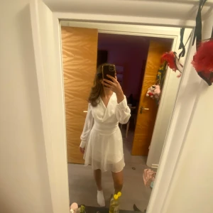 Vit student klänning - Säljer en elegant vit studentklänning med långa ärmar och v-ringad design. Klänningen har en flödande kjol och är perfekt för en stilren look. Använt den bara en gång på min student 