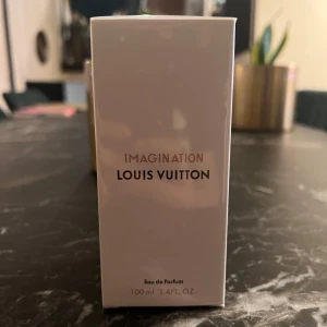 Imagination Eau de Parfum från Louis Vuitton - Säljer en elegant flaska av Imagination Eau de Parfum från Louis Vuitton. Flaskan rymmer 100 ml och har en stilren design med en klarblå vätska. Perfekt för den som söker en lyxig doftupplevelse. Flaskan har en svart kork med Louis Vuittons logotyp.