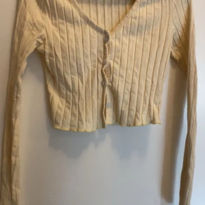 Gul ribbad kofta - Säljer en söt gul ribbad kofta med v-ringning och knappar framtill. Den är croppad och har långa ärmar, perfekt för lager på lager-stil. Passar bra till både jeans och kjol! Den är i nyskick från Shein i storlek S