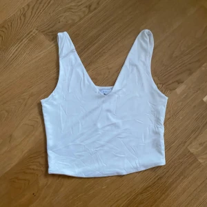 Vit ärmlös linnetopp - Säljer en stilren vit ärmlös linnetopp med djup v-ringning. Perfekt för varma dagar eller som ett basplagg i garderoben. Enkel och mångsidig design som passar till det mesta.