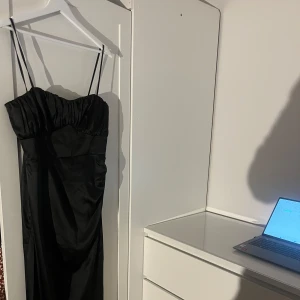 Svart axelbandslös klänning - Elegant svart klänning med smala axelband och en figurnära passform. Oanvänd. 