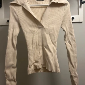 Beige ribbad tröja - Säljer en stilren beige ribbad tröja med krage och v-ringning. Tröjan har långa ärmar och en figurnära passform. Perfekt för en chic och avslappnad look.