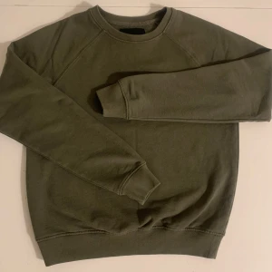 Sweatshirt  - Säljer en stilren olivgrön sweatshirt från lager 157. Tröjan har en klassisk rund halsringning och långa ärmar med ribbade muddar. Perfekt för en avslappnad look. 