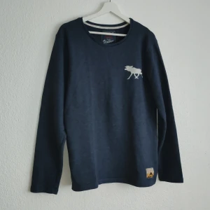 Mörkblå långärmad tröja från Bondelid - Säljer en stilren mörkblå långärmad tröja från Bondelid med ett litet tryck av en älg på bröstet. Tröjan har en rund halsringning och en liten etikett nertill. Perfekt för en avslappnad stil.