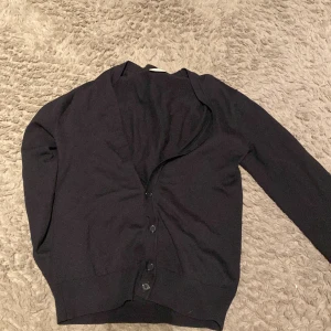 Svart cardigan - Säljer en stilren svart kofta från John Henric. Koftan har långa ärmar och knappar framtill, perfekt för en elegant look. Passar bra till både vardag och mer uppklädda tillfällen.