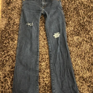 Blå bootcut jeans med håll - Snygga blå stockholm stil bootcut jeans med snygga hål på framsidan. Perfekta nu för våren.. De har en klassisk femficksdesign och en bekväm passform. Säljer pågrund av att dom ej kommer till andvändning längre💗