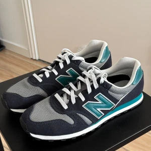 New Balance sneakers i grå och turkos - Snygga New Balance sneakers i en kombination av grått och grönt. Skorna har en klassisk design med snörning och den ikoniska 'N' loggan på sidan. Perfekta för en avslappnad stil.