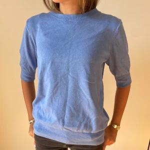 Blå stickad T-shirt - Säljer en stilren blå tröja med trekvartsärm. Perfekt för en avslappnad look. Tröjan har en rund hals och ribbade kanter vid ärmslut och nederkant.