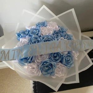 Blå och vit ros bukett - Vacker bukett med konstgjorda rosor i blått och vitt, insvept i transparent papper. Perfekt som en romantisk gest eller dekoration. Bandet har texten 'MIN EVIGA KÄRLEK' i silver. (Köpta från instagram, lite över 700kr)