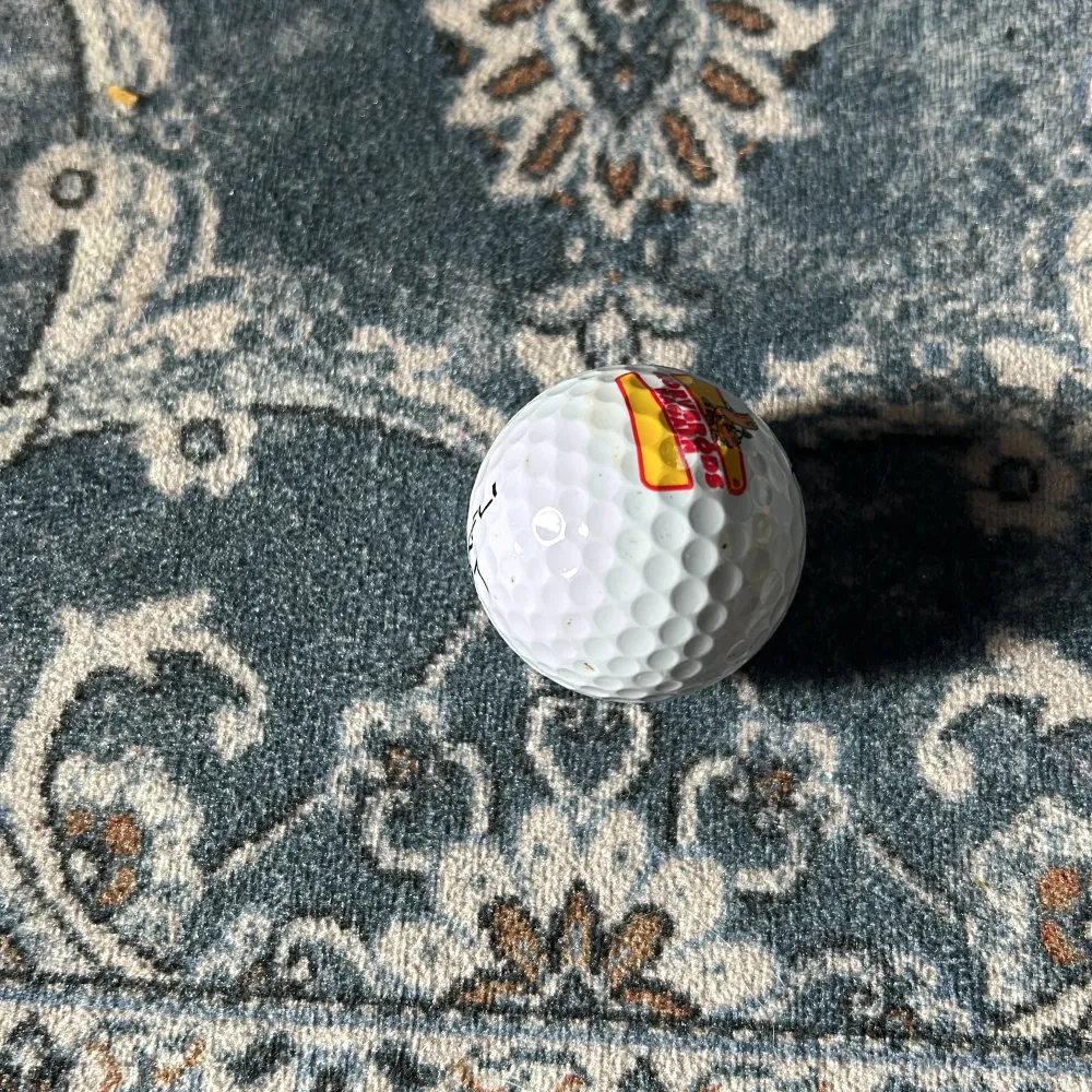 Säljer en vit golfboll från Maxfli med en unik korvbröds logga. Bollen har texten 'TOUR FIRE' och siffran 7 tryckt på sig. Perfekt för golfentusiaster som vill ha något annorlunda på banan! 🏌️♂️. Muu.