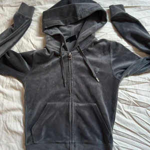Grå zip tröja från Juicy Couture - Säljer en snygg grå hoodie från Juicy Couture i mjukt material. Hoodien har dragkedja och en broderad logga på bröstet. Lite rostig på dragkedjan men inget som syns, metallen på högra snöret har gått av men annars är den som ny!💕storlek xs
