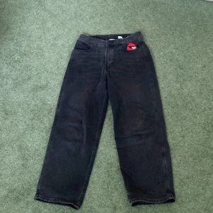 Svarta jeans med Angry Birds-märke - Säljer ett par svarta jeans med en cool Angry Birds-brodering på fickan. Byxorna har en rak passform och är perfekta för en avslappnad stil. De har en klassisk femficksdesign och är tillverkade i ett slitstarkt material.