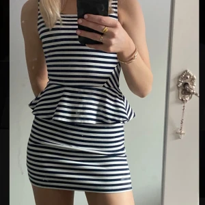 Randig peplumklänning i marinblått och vitt - Säljer en tight, ärmlös kortklänning med marinblå och vita ränder. Klänningen har peplumvolang i midjan och dragkedja i ryggen.🦓