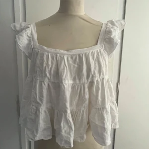 Vit volangig blus från SHEIN - Säljer en söt vit blus från SHEIN i storlek XS. Toppen har breda axelband, volanger och är tillverkad i ett tunt, luftigt tyg. Perfekt för varma dagar och ett jättebra plagg till sommaren 