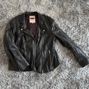 Svart skinnjacka från Part Two - Säljer en svart skinnjacka från Part Two med klassisk bikerstil. Jackan har långa ärmar, sned dragkedja framtill och dragkedjor vid fickorna. Snygg passform och stilren design som lyfter varje outfit.
