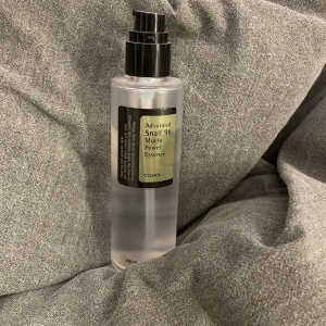 COSRX Advanced Snail 96 Mucin Power Essence - En genomskinlig pumpflaska med COSRX Advanced Snail 96 Mucin Power Essence. används för att återfukta och stärka huden. Perfekt för dig som vill ha extra glow och mjukhet i din hudvårdsrutin.