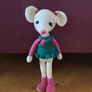 Handgjord virkad mus med klänning och rosetter - Supergullig handvirkad mus med stora öron, klädd i en turkos klänning med rosa detaljer och små röda rosetter. Musen har rosa skor och rosa armar, samt broderade ögon och nos. Perfekt som accessoar eller dekoration.