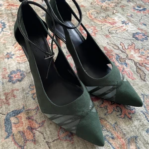 Gröna klackskor med spetsig tå - Snygga gröna klackskor med spetsig tå och smal klack. Skorna har en elegant snörning runt ankeln och dekorativa detaljer på sidan. Bra skick med undantag för två små repor som går att se på bilderna, påverkar dock inte helhetsintrycket. Använd 2-3 gånger.   