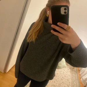 Grå stickad tröja - Säljer en mysig grå stickad tröja med polokrage. Tröjan har långa ärmar och en lös passform, perfekt för kyligare dagar. Den ribbade strukturen ger en extra touch av stil. Passar bra till både jeans och leggings.