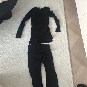 Svart ribbad långärmad topp och byxor - Säljer en svart ribbad långärmad topp med matchande byxor. Toppen har en v-ringad design och byxorna har en elastisk midja för extra komfort. Perfekt set för en stilren look.