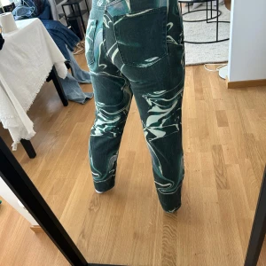 Gröna swirlmönstrade jeansbyxor Weekday - Unika jeansbyxor med grönt och vitt swirlmönster. Byxorna har normal passform, raka ben och klassisk femficksdesign med dragkedja och knapp. Materialet är denim och mönstret ger en cool statement-look. Säljer för att de är lite korta i benen för min smak och jag är 168. Skulle passa någon som är lite kortare. Dom är från Weekday. Använda 1 gång. Passar storleken 34-36