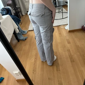Grå cargopants från Gina Tricot - Säljer ett par grå cargopants från Gina Tricot med raka ben och flera fickor på sidorna. Byxorna har normal passform, dragkedja och knapp i midjan samt bälteshällor. Perfekta för en avslappnad stil. Som ni ser får jag inte på mig dom. Dessa är i storlek 34. Använda 1 gång