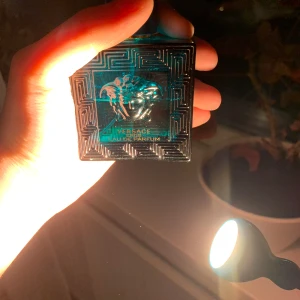 Versace Eros Eau de Parfum 50ml - Versace Eros Eau de Parfum i en lyxig blågrön glasflaska med guldlock och ikoniskt Medusahuvud på framsidan. Flaskan har geometriskt mönster och kommer med originalkartong i blått och guld. Volym: 50 ml.