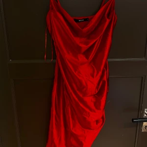 Röd satinklänning  - Säljer en röd satinklänning från bikbok  med smala axelband. Klänningen har en elegant cowl-neck och är figurnära med en kort längd. Perfekt för dig som vill sticka ut!