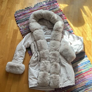 Vit vinterjacka med stor pälskrage och pälskanter - Säljer en vit vinterjacka med stor fluffig pälskrage och pälskanter vid ärmsluten. Jackan har dragkedja och knappar framtill samt fickor på sidorna. Passar storlek S och M. Is prinsessa👑❄️