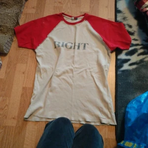 Beige och röd t-shirt med tryck - T-shirt i beige med röda ärmar och krage. Trycket 'RIGHT' i grått på bröstet. Klassisk basebollstil med kontrastfärgade raglanärmar. Perfekt för en avslappnad look.