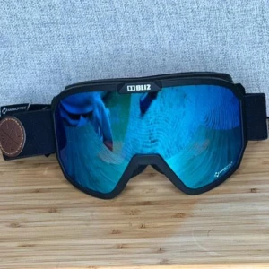 Blå skidglasögon från Bliz - Snygga skidglasögon från Bliz med blå spegelglas och svart ram. Justerbart band med Bliz-logga och Nanoptics-teknologi. Perfekta för vinterns äventyr i backen.