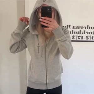 Grå hoodie med dragkedja - Säljer en stilren grå hoodie med dragkedja och luva. Perfekt för en avslappnad look. Den har långa ärmar och ribbade muddar vid ärmslut och nederkant.