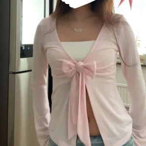 Rosa långärmad topp med knyt - Säljer en söt rosa långärmad topp med knyt framtill. Toppen har en v-ringad design och är perfekt för en avslappnad stil. Den är tillverkad i ett mjukt material som ger en bekväm passform.