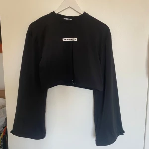 Svart croppad tröja från Madlady - Säljer en svart croppad tröja från Madlady. Tröjan har långa ärmar och justerbara snören vid ärmsluten. Storlek s bara använd en gång