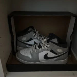 Nike sneakers i grått och vitt - Snygga Nike sneakers i grått och vitt med klassisk design. Skorna har en svart Nike-logga på sidan och vita snören. Perfekta för en stilren look.