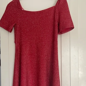 Röd glittrig klänning - Säljer en jättefin röd glittrig klänning med korta ärmar och en smockad överdel. Den är från Cubus storlek 157-164