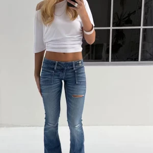 Blå bootcut jeans - Snygga blå bootcut jeans med låg midja och slitdetaljer på framsidan. Helt nya med prislappen kvar är storlek m