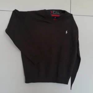 Grå tröja från Polo Ralph Lauren - Säljer en stilren grå tröja från Polo Ralph Lauren med klassisk v-ringning och det ikoniska logotypbroderiet på bröstet. Perfekt för en avslappnad men ändå elegant look.