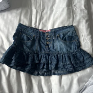 Jeanskjol med volang - Säljer en snygg jeanskjol från Rebels Forever med volangdetaljer och knappar framtill. Super söt och perfekt till sommaren! Kom privat vid frågor❤️ 36cm rakt över i midjan
