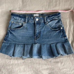 Jeanskjol med volangkant - Säljer en blå jeanskjol från 157 med volangkant nedtill. Kjolen har klassiska jeansfickor fram och bak, knapp och dragkedja i midjan samt råa kanter längst ner för en cool look.