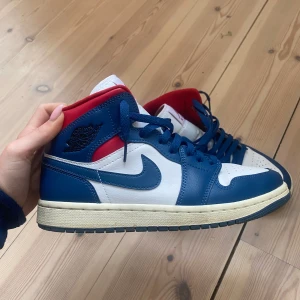 Nike Air Jordan 1 mid - Säljer ett par Nike Air Jordans 1 mid, blå, vit och röd. Jättebra skick och fräscha inuti och utanpå! Har lite crease men inga andra defekter. 