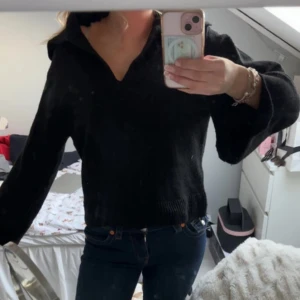 Svart stickad tröja med krage - Säljer en svart stickad tröja med krage och v-ringning. Tröjan har långa ärmar och en avslappnad passform, perfekt för kyligare dagar. Passar bra till jeans eller kjol för en stilren look.